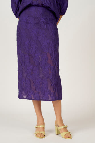 Jupe longue violette d'Astrid Black Label, avec un imprimé floral texturé et associée à des mules à talon jaune clair.