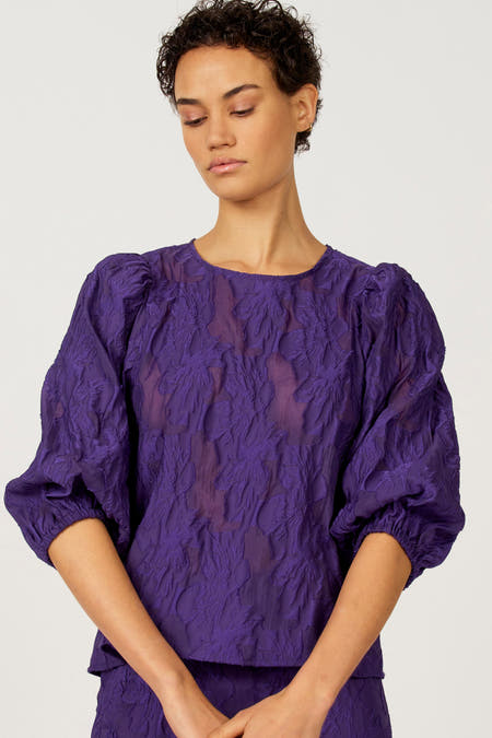 Chemisier violet à manches trois-quarts d'Astrid Black Label, avec un motif floral texturé et un détail en trou de serrure au dos.