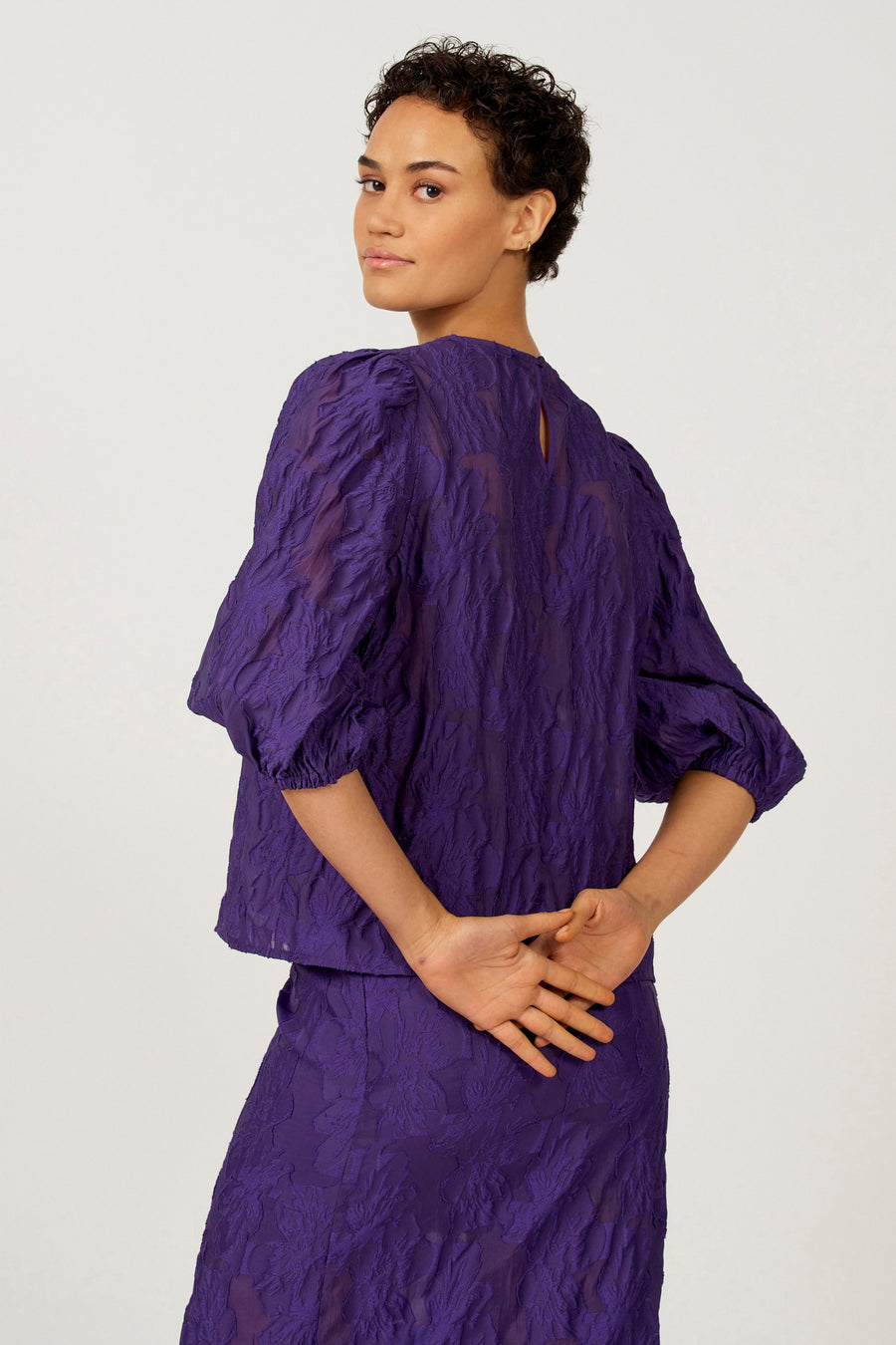 Paarse blouse met driekwart mouwen van Astrid Black Label, met een getextureerd bloempatroon en een sleutelgat detail aan de achterkant.