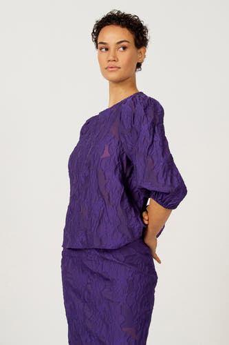 Chemisier violet à manches trois-quarts d'Astrid Black Label, avec un motif floral jacquard et des manches bouffantes.