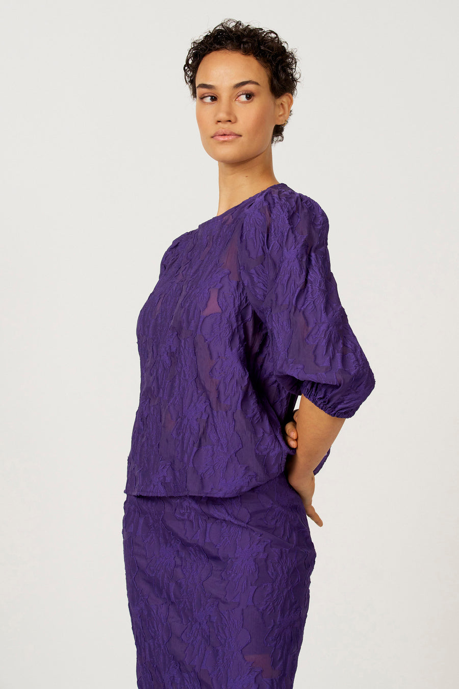 Chemisier violet à manches trois-quarts d'Astrid Black Label, avec un motif floral jacquard et des manches bouffantes.
