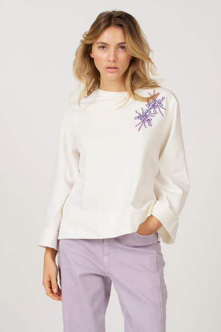 T-shirt écru à manches longues d'Astrid Black Label, avec des manches larges et un col rabattu, associé à une jupe violette.