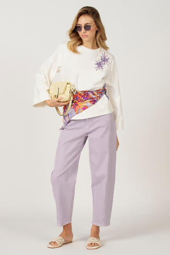 T-shirt écru à manches longues d'Astrid Black Label, avec des décorations violettes et un foulard autour de la taille.