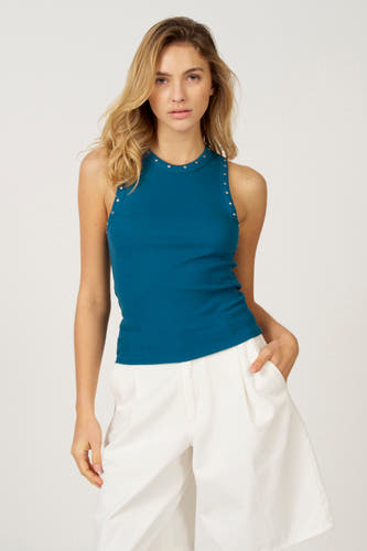 T-shirt bleu Astrid Black Label avec des boutons sur les manches, porté avec un pantalon blanc.