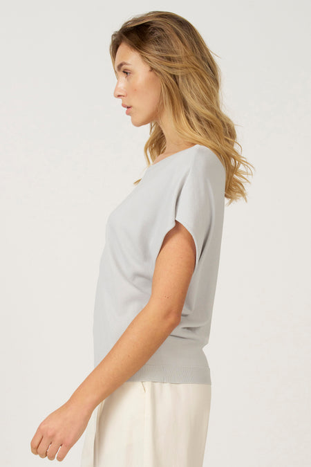 Vrouw in grijze top en crèmekleurige broek, zijdelings.