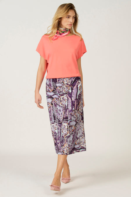 Vrouw in koraalkleurige top en paarse rok met print, lichte hakken.