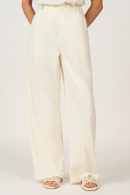 Jean blanc d'Astrid Black Label, avec des jambes larges et une taille haute, porté avec des sandales.