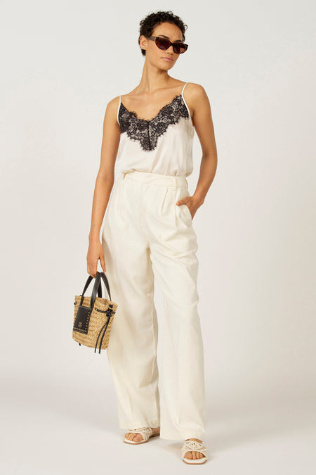 Vrouw met zonnebril, witte top met kant, witte broek en zomerse handtas.