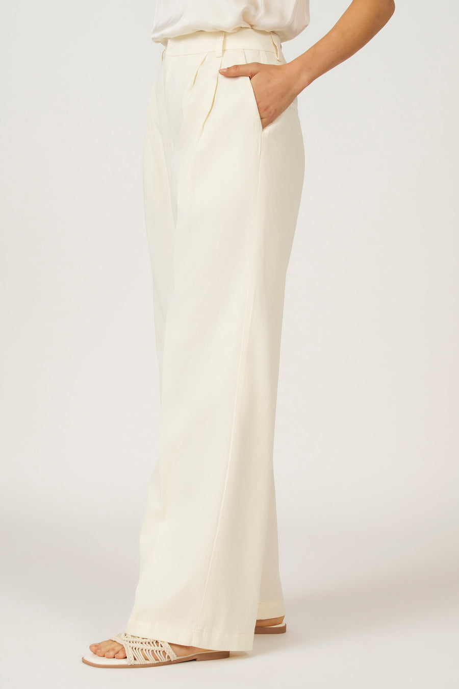 Gebroken witte, wijde pantalon met plooien en steekzakken, gecombineerd met een top en sandalen.