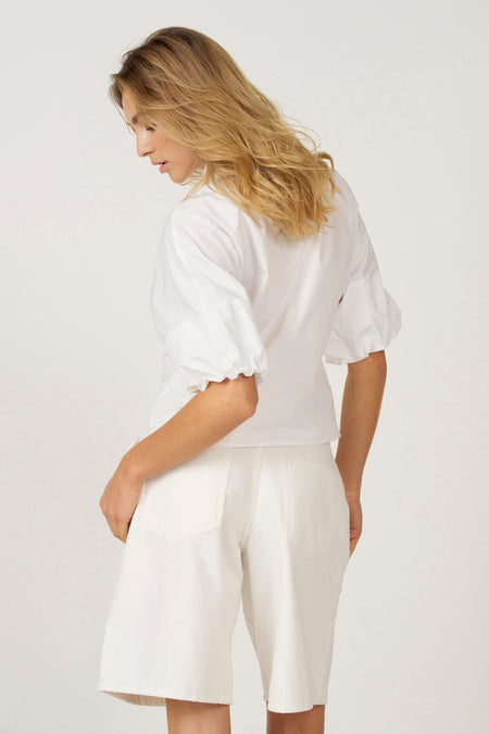 Blouse blanche d'Astrid Black Label avec des manches trois-quarts, vue de derrière, associée à une jupe blanche.