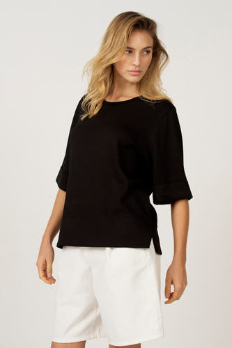 T-shirt noir à manches courtes d'Astrid Black Label, avec des manches retroussées et porté avec un pantalon blanc.