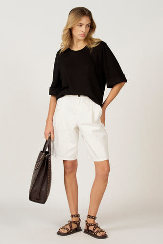 T-shirt noir à manches courtes d'Astrid Black Label, avec des manches retroussées, associé à des short blancs et des sandales en cuir et un sac.
