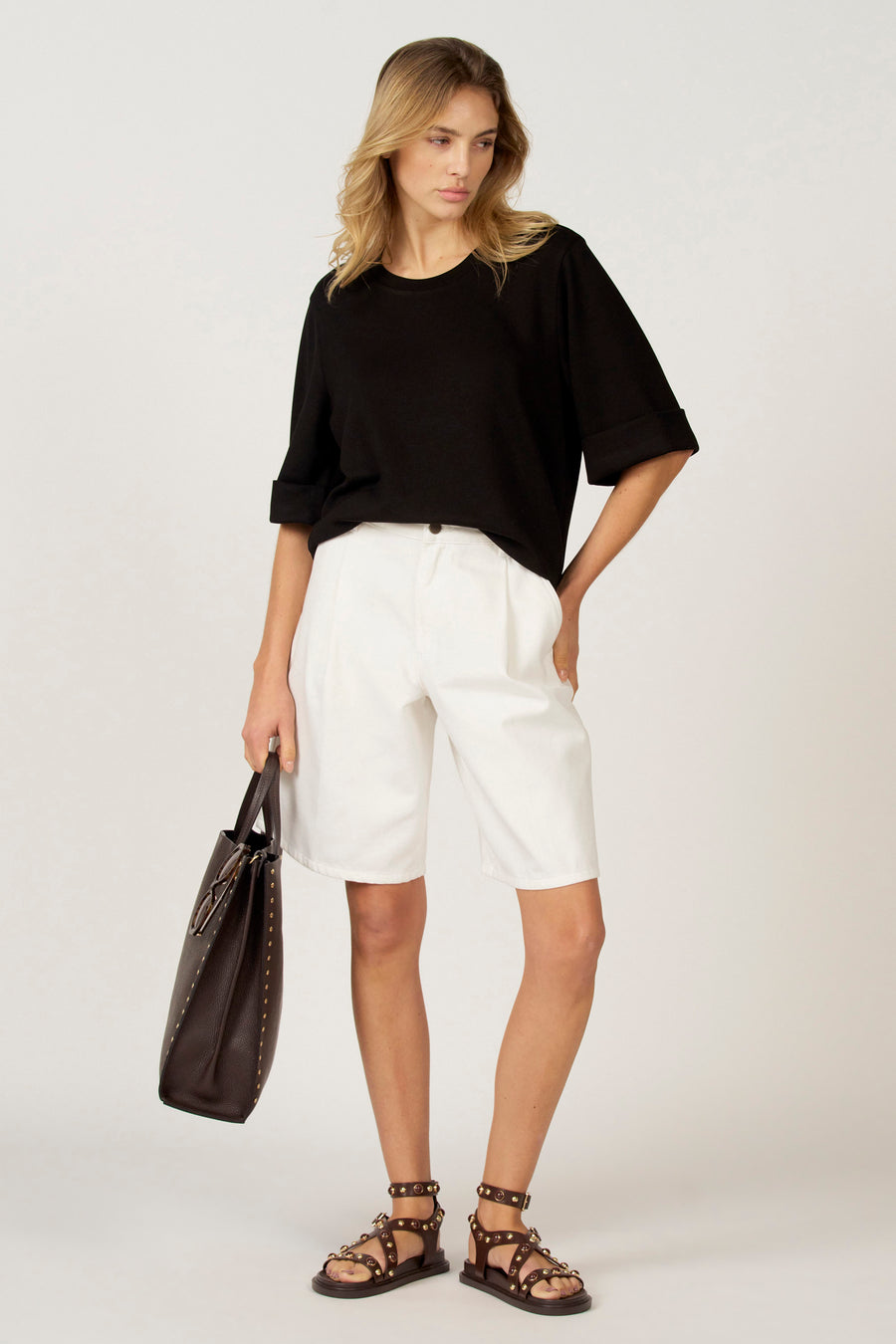 Zwart T-shirt met korte mouwen van Astrid Black Label, met omgeslagen mouwen, gecombineerd met witte shorts en leren sandalen en tas.