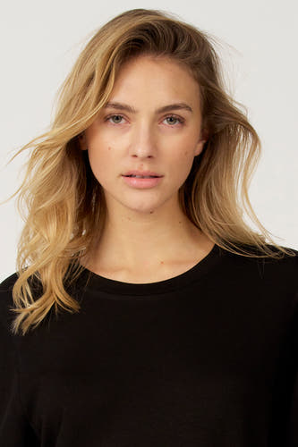 T-shirt noir à manches courtes d'Astrid Black Label, porté avec des cheveux blonds lâches.