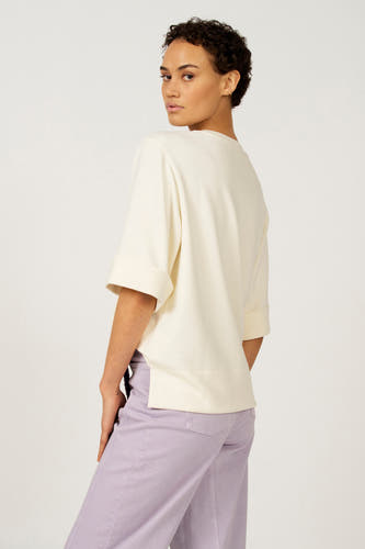 Ecru T-shirt met korte mouwen van Astrid Black Label, met omgeslagen mouwen en zijsplit, gecombineerd met een lila broek.
