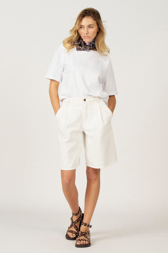 T-shirt blanc à manches courtes d'Astrid Black Label, avec un foulard autour du cou et une short blanc.