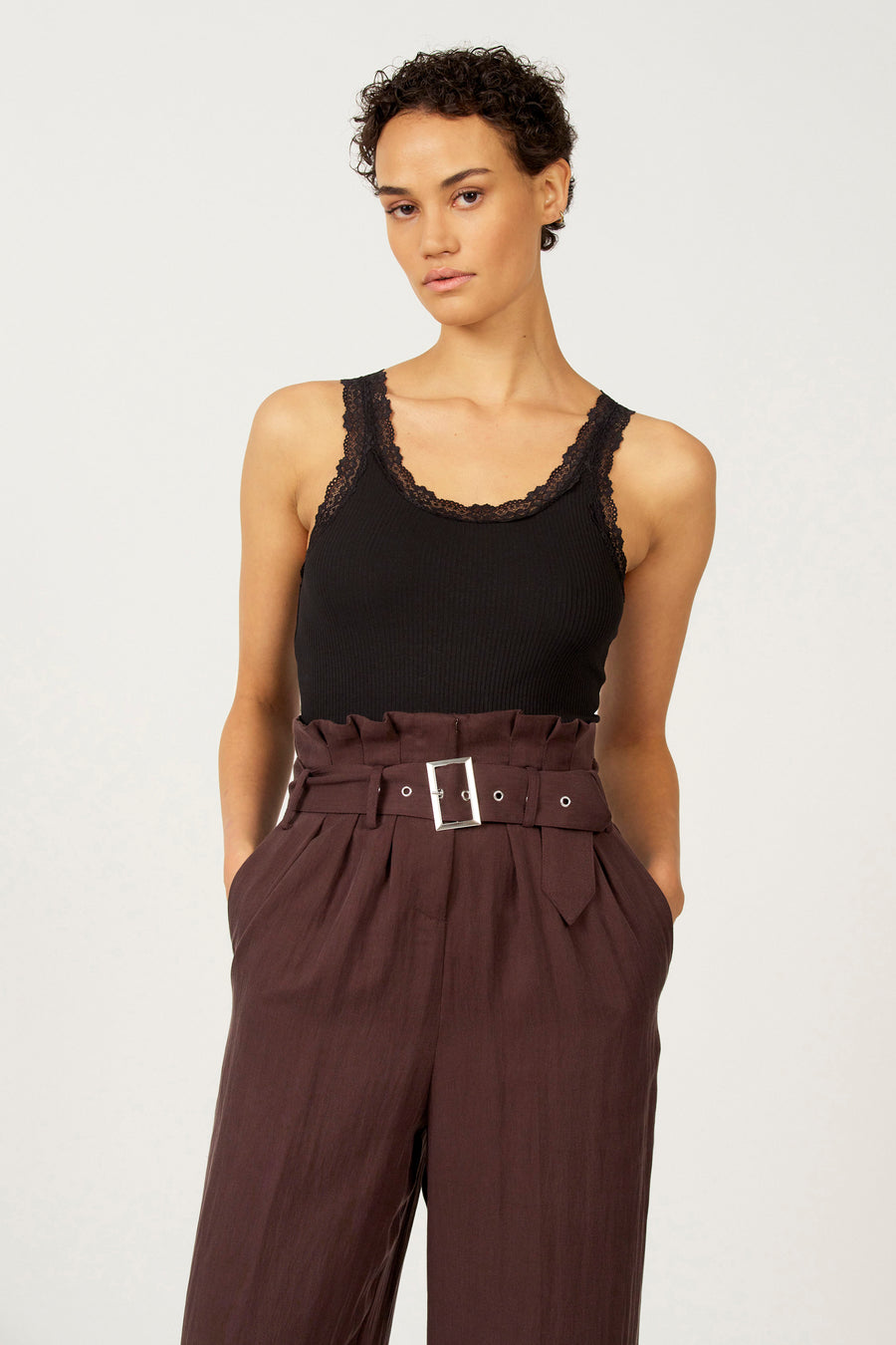 Zwarte singlet van Astrid Black Label met kanten details rond de halslijn, gecombineerd met bruine high-waisted broek.