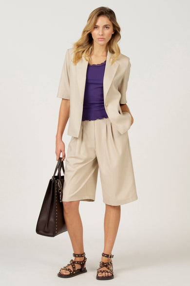 Robe simple noire d'Astrid Black Label, portée sous un blazer beige et des bermudas coordonnés, avec des sandales brunes et une grande sacoche.