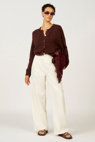 Model met bruin vest, witte broek en rode tas.