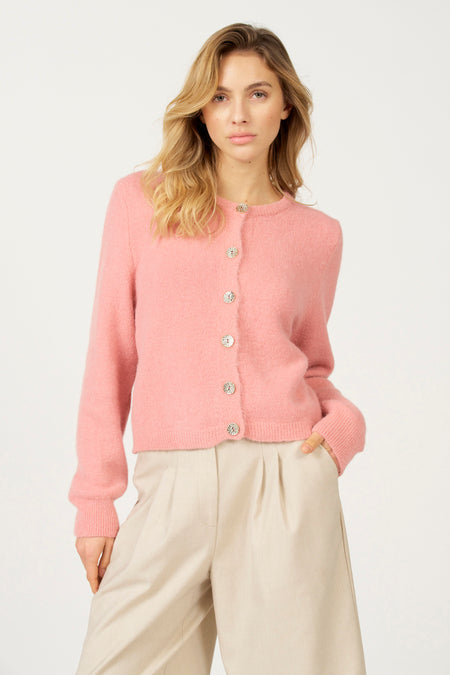 Model draagt roze vest met beige broek tegen witte achtergrond.