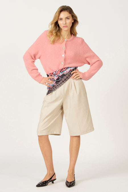 Model met roze vest en beige bermuda's, staand tegen een witte achtergrond.