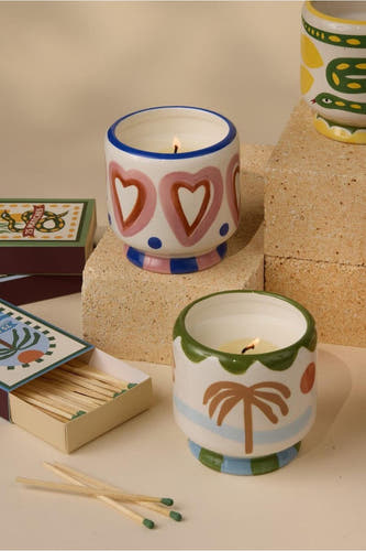 Des bougies multicolores de PADDY WAX, avec divers motifs et détails décoratifs, à côté de boîtes à allumettes.