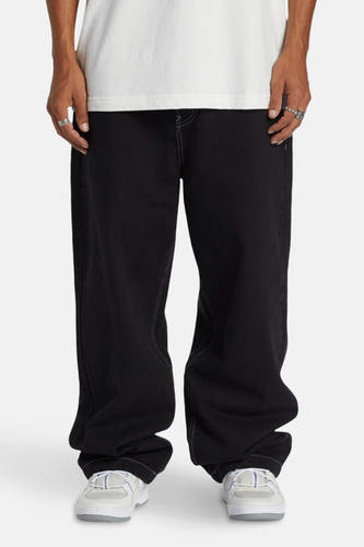 Jean délavé noir de DC SHOES, avec des surpiqures contrastantes et associé à un T-shirt blanc et à des baskets.