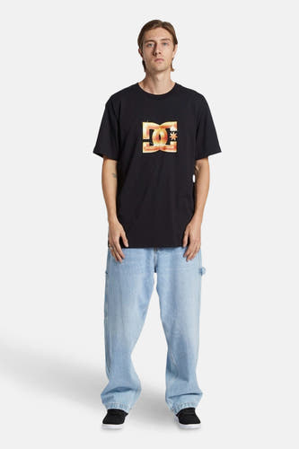 Jean denim bleu clair large de DC Shoes, porté avec un t-shirt noir à logo et des chaussures noires.