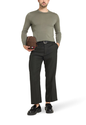 Staande man in groene trui en donkere broek met bruine tas.