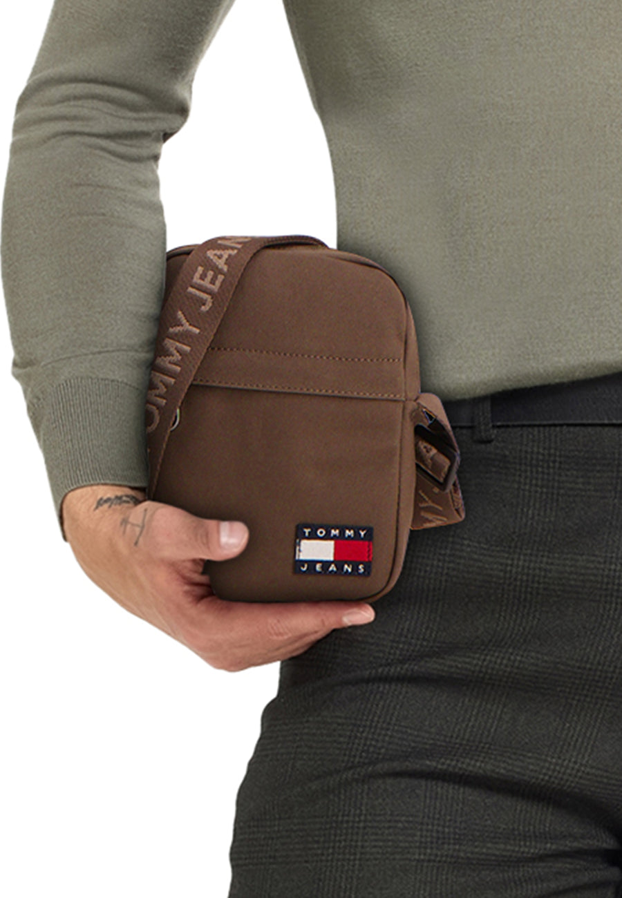 Persoon met bruine Tommy Jeans crossbodytas, groene trui en grijze broek.