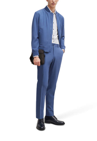 Sac à dos noir de TOMMY JEANS, porté par un homme en bleu de travail avec une chemise blanche imprimée et des chaussures noires.