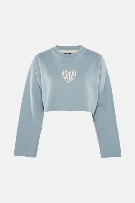 Gilet turquoise de KAOTIKO, avec un logo brodé en forme de cœur sur la poitrine, modèle cropped.
