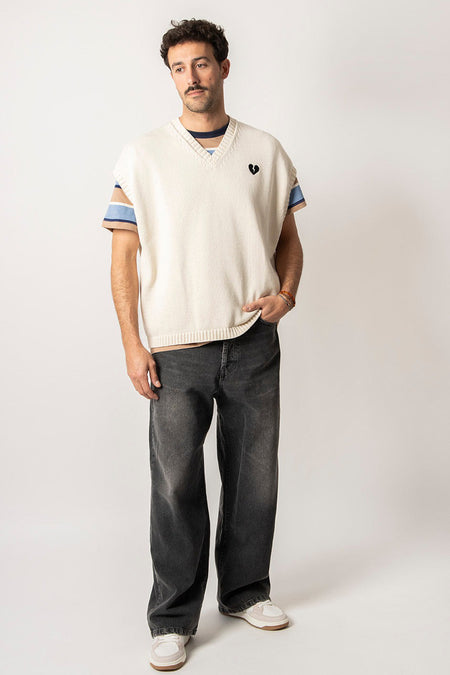 T-shirt écru de KAOTIKO avec détail de cœur brisé et t-shirt rayé en dessous, associé à des jeans gris et des baskets blanches.