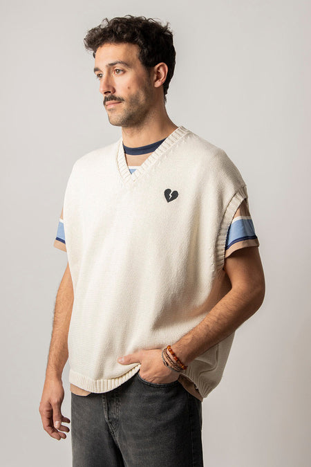 T-shirt écru de KAOTIKO avec détail de cœur brisé, porté sur un t-shirt rayé et un jean noir.