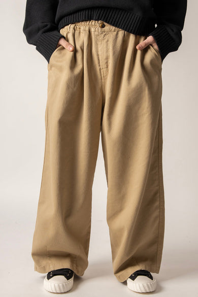 Beige broek van KAOTIKO met wijde pijpen, elastische tailleband en steekzakken, gedragen met een zwarte trui en sneakers.
