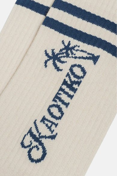 Chaussettes écru de KAOTIKO avec des rayures bleu foncé, un palmier et le nom de la marque en bleu.