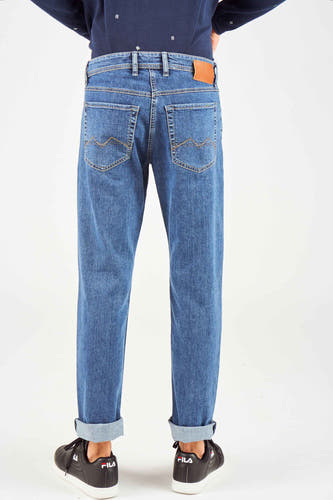 Jean bleu moyen droit de MAC avec des poches repliées et des chaussures noires visibles.