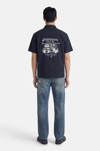Chemise bleue à manches courtes de KAOTIKO, avec imprimé blanc Café de Paris au dos, à combiner avec un jean.