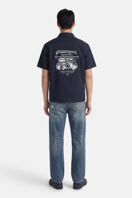 Chemise bleue à manches courtes de KAOTIKO, avec imprimé blanc Café de Paris au dos, à combiner avec un jean.
