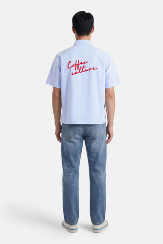 Chemise bleue à rayures à manches courtes de KAOTIKO, avec imprimé rouge au dos, à combiner avec un jean et des baskets.