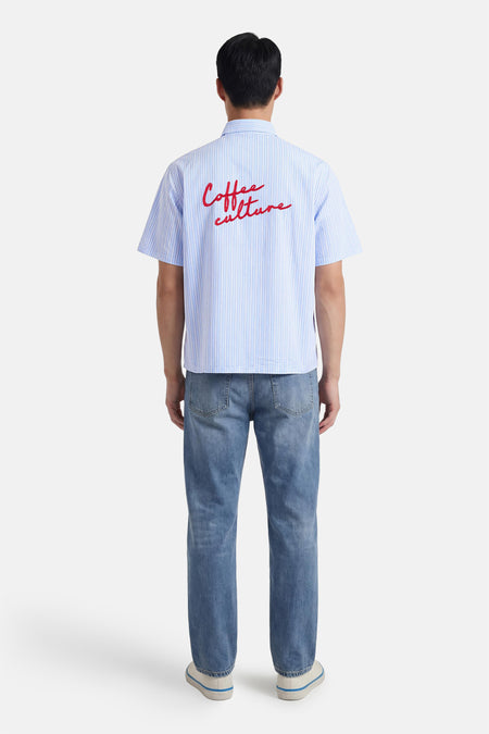Chemise bleue à rayures à manches courtes de KAOTIKO, avec imprimé rouge au dos, à combiner avec un jean et des baskets.
