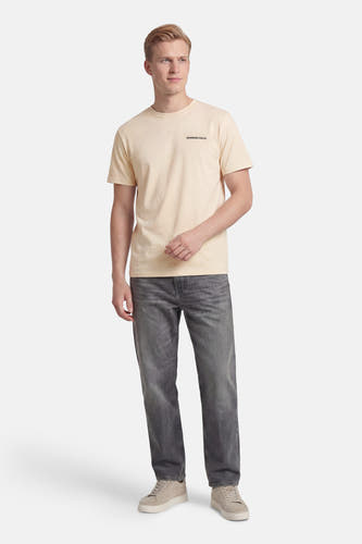 T-shirt écru à manches courtes de KAOTIKO avec le texte noir "Morning Calls." en haut à droite. Habillé avec un jean gris et des baskets claires.
