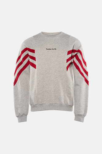 Pull gris de KAOTIKO, avec col rond et rayures rouges sur les manches, combiné avec un jean foncé et des chaussures grises.