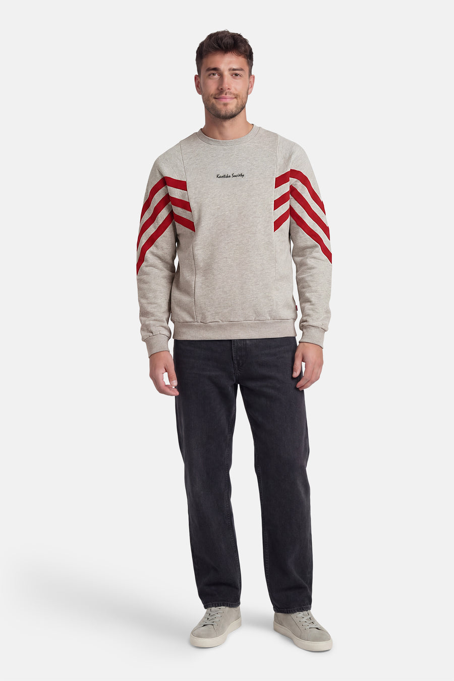 Grijze sweater van KAOTIKO, met ronde hals en rode strepen op de mouwen, gecombineerd met een donkere jeans en grijze schoenen.
