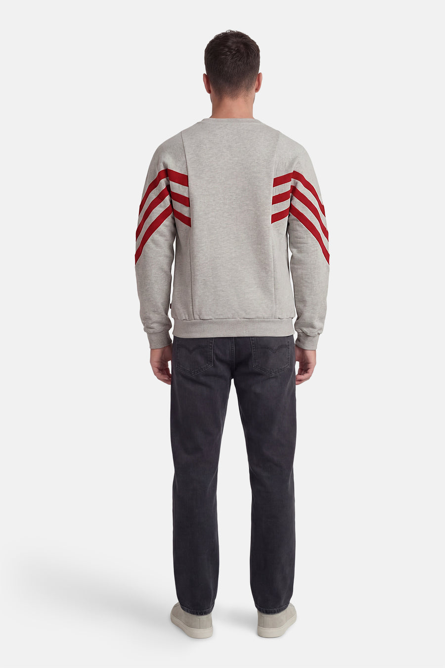 Grijze sweater met ronde hals van KAOTIKO, met rode strepen op de mouwen, gecombineerd met donkere jeans en lichte schoenen, achteraanzicht.

