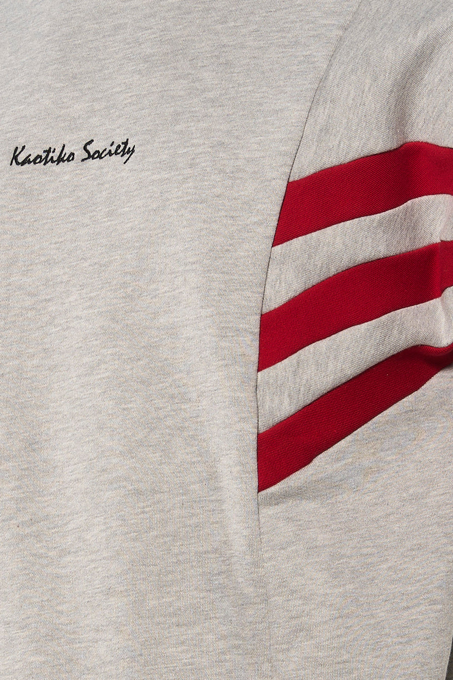 Pull gris de Kaotiko à manches longues et rayures rouges sur la manche.