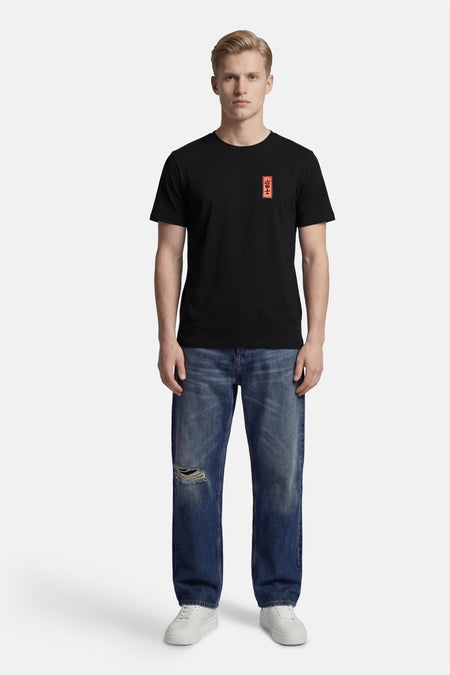 T-shirt noir à manches courtes de KAOTIKO, avec un petit écusson rouge, combiné avec un jean bleu et des baskets blanches.