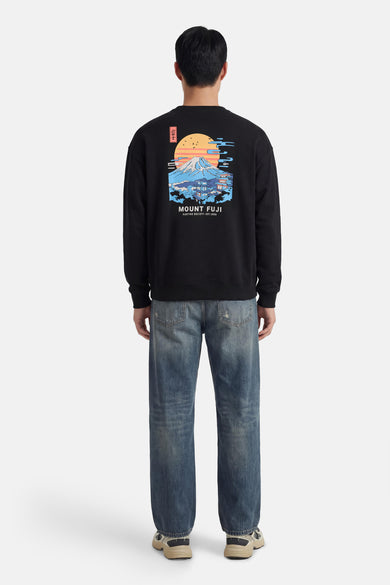 Pull noir de KAOTIKO avec une image du Mont Fuji au dos, combiné avec un jean bleu et des baskets couleur crème.