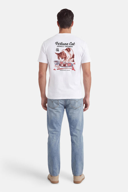 T-shirt blanc de KAOTIKO, avec un imprimé de chat et de sushis au dos, porté avec un jean bleu et des chaussures en daim.