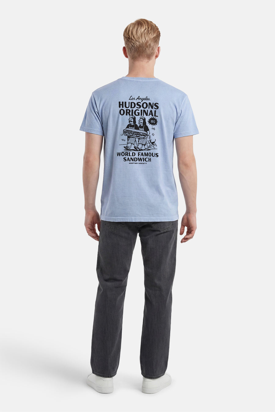 T-shirt bleu clair de KAOTIKO avec un grand imprimé graphique noir au dos de deux personnages portant un sandwich, porté par un homme avec un pantalon gris foncé et des baskets blanches.
